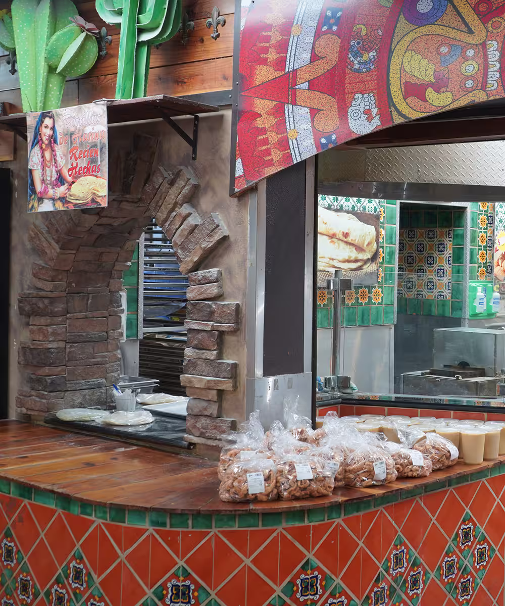 Interior of a colorful Mexican eatery with decorative tiles and a vibrant mural of an Aztec calendar