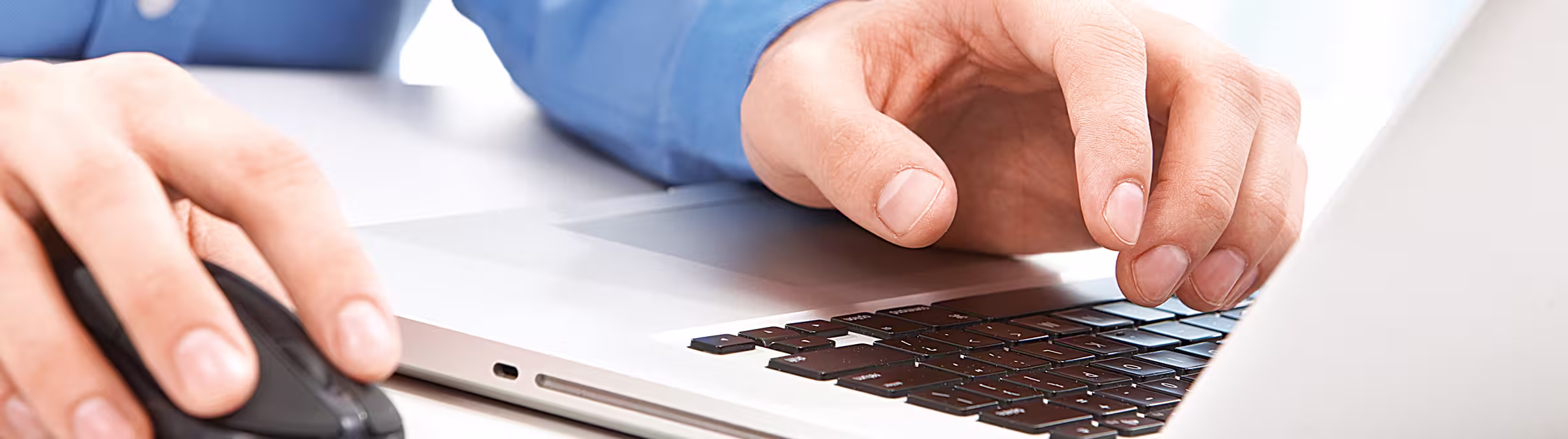 Person's hands using a laptop and mouse on a white desk
